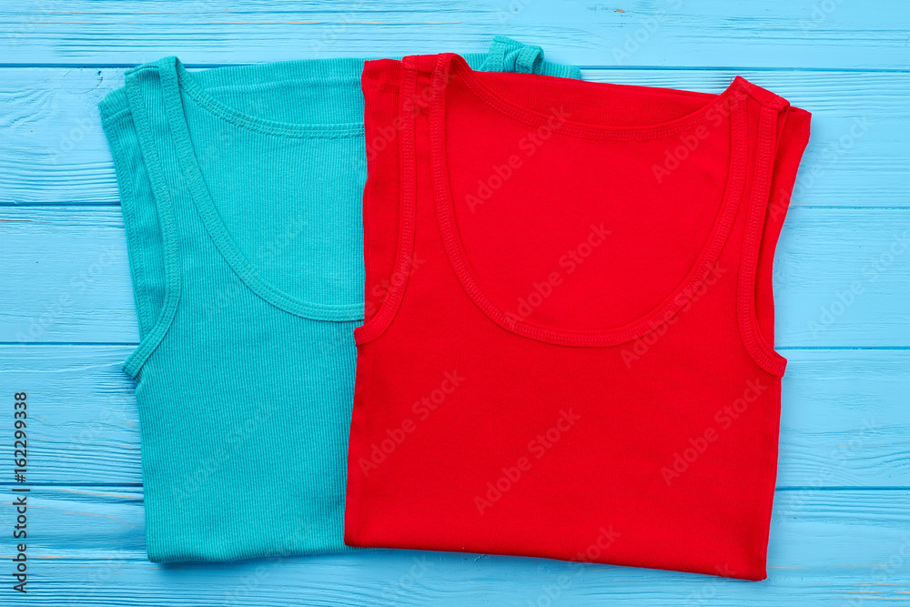 Two colored t-shirts, wooden background. Colored summer clothing for youth close up.