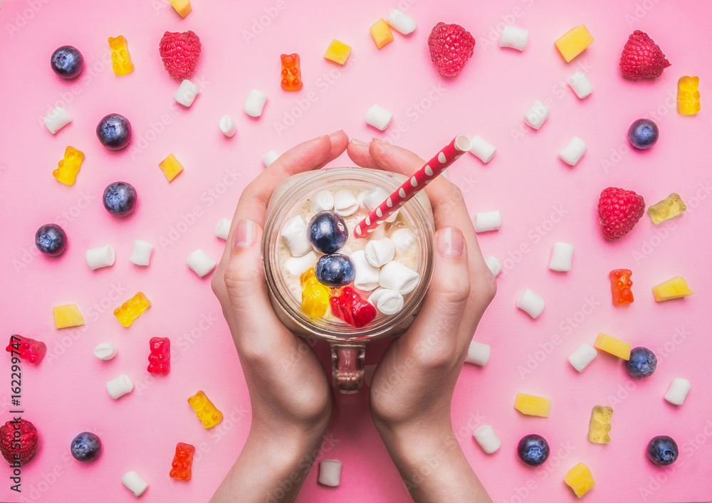 girl holding a fresh smoothie with raspberry, kiwi and bananas on a pink background, with the expansion around the multicolored hearts, berries, jelly and marshmallow healthy food, valentines day