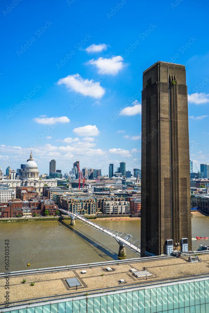 Fototapeta premium The old chimney of the Tate Modern Gallery on the right. St.Paul's Cathedral in the distance on the left and the Millennium walkway bridge. London UK. 