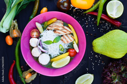 Traditional thai green curry with grilled chicken, lime, funchoza noodles and vegetables, served in bright plate, decorated with daicon, chili peppers,sesame,lime and spices, delicious thai cuisine photo