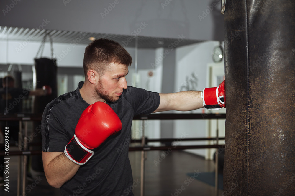 A young man is boxing in the hall. attentive sportsman in the boxing hall practicing boxing punches during training