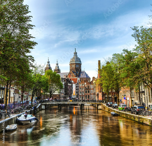 The most famous canals and embankments of Amsterdam city during sunset. General view of the cityscape and traditional Netherlands architecture.