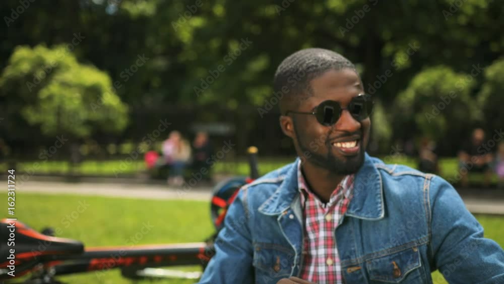 Close up portrait of young african student using tablet in the park while sitting on the grace on background with bikecycle and green tree. Close up portrait of young african student using tablet in the park while sitting on the grace on background with bikecycle and green tree.