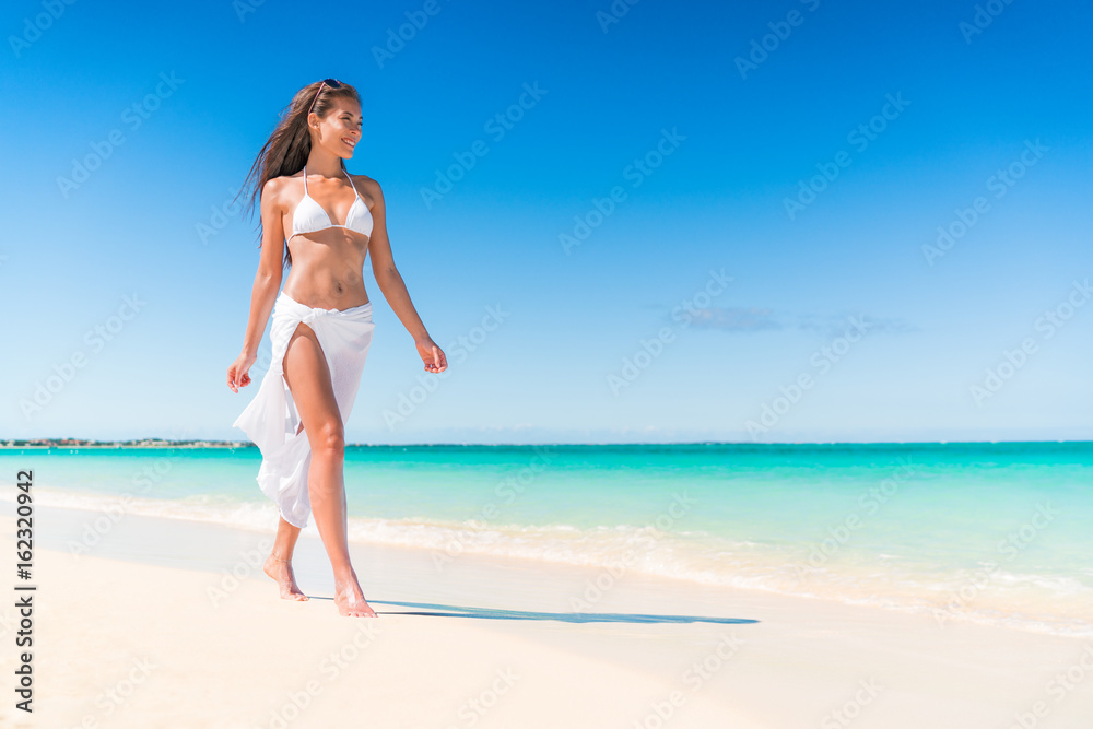 Luxury beach travel vacation swimwear woman relaxing walking on white sand in beachwear cover-up. Asian girl on tropical destination paradise wearing pareo fashion swimwear.