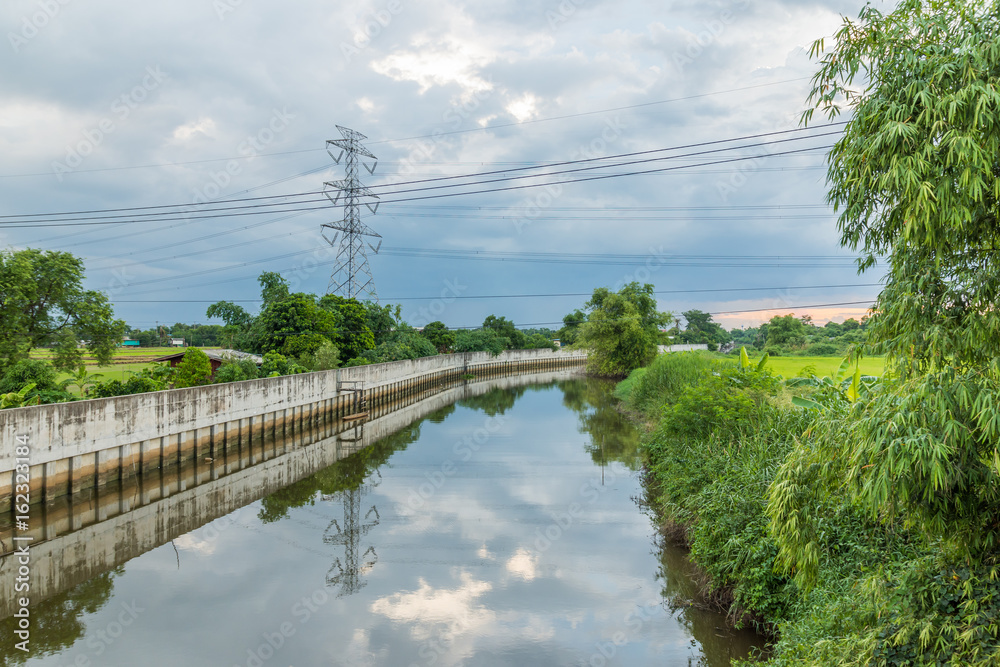 Landscape of  Flood protection wall with Wooden boats reflections in the water and trees on blue sky.