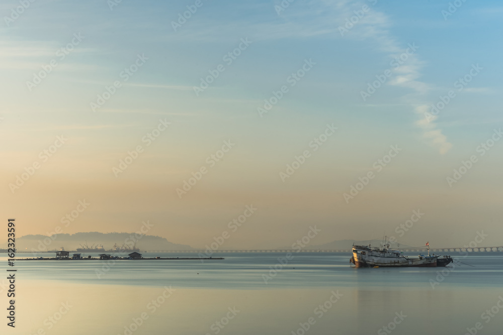 A fishing boat is mooring in the calm sea in a serene morning.