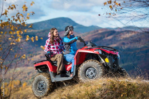 Happy females ATV driver in winter clothing on snowy hills on the background of mighty mountains and trees with yellow leaves