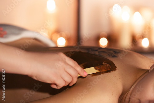 Beautiful girl having chocolate facial mask apply by beautician.