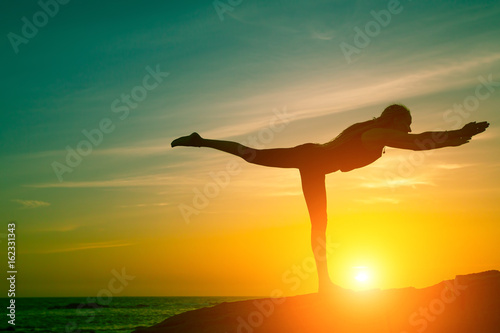 Fototapeta Naklejka Na Ścianę i Meble -  Yoga and healthy lifestyle. Silhouette of fitness woman doing exercises on the sea beach during amazing sunset.