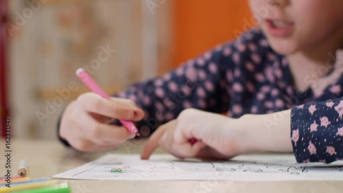 Girl using a pink felt-tip pen draws on paper photo
