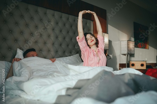 Fashion photo of two young beautiful lovers relax at the hotel on a bed,they are smiling photo