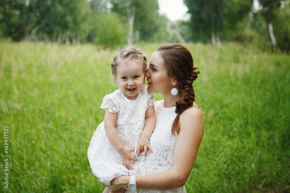 Young mother with daughter on hands in the same white dresses in the Park. Family Look Young mother with daughter on hands in the same white dresses in the Park. Family Look