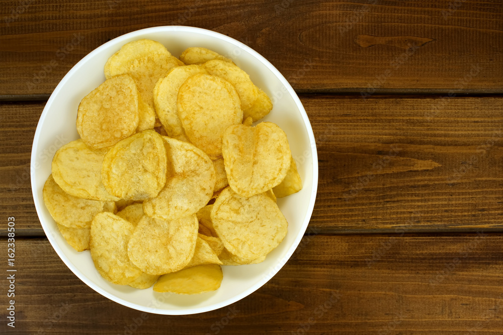 Potato chips in bowl on a wooden background, top view