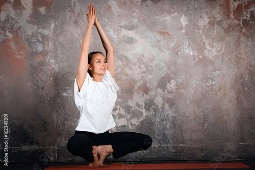 Yoga meditating young woman urban style, gray background, indoor, copy space, gray wall, praying hands