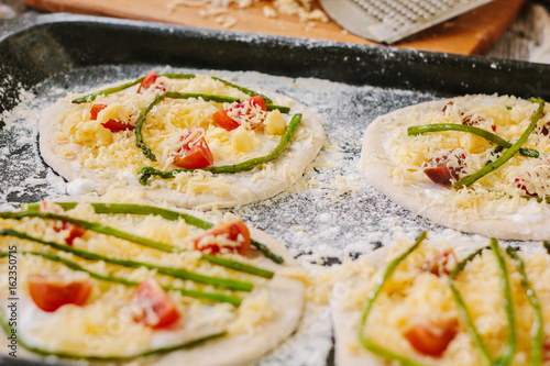 Cooking process of making mini pizza - small and personal, with cheese, tomatoes and asparagus.