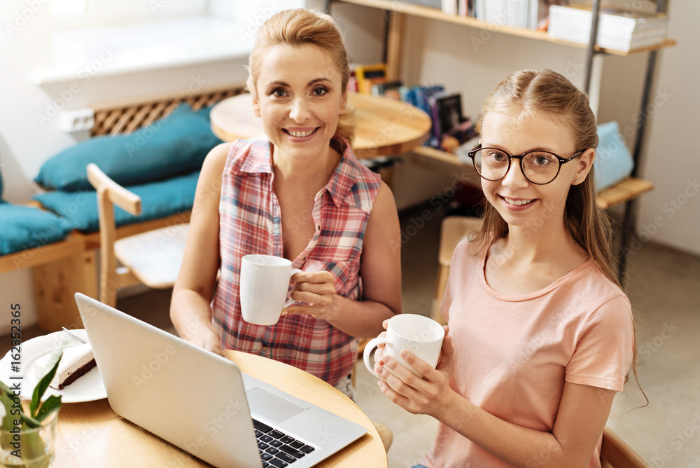 Happy mother and daughter posing with coffee mugs