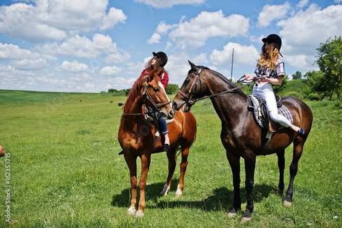 Tow young pretty girls riding a horses on a field at sunny day © AS Photo Family