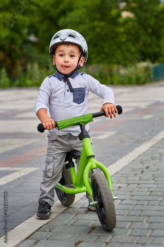 Child boy in white helmet riding on his first bike with a helmet. Bike without pedals. © Aleksey