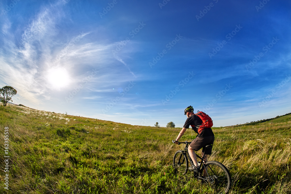 Young cyclist riding mountain bicyclist against beautiful sunrise in the countryside.