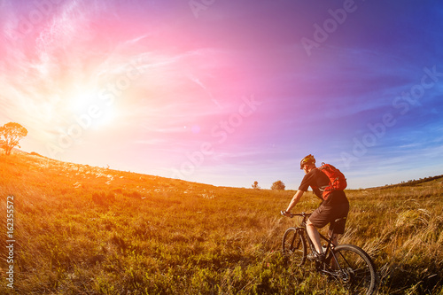 Young cyclist riding mountain bicyclist against beautiful sunrise in the countryside.