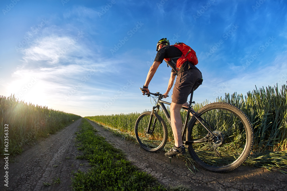 Cyclist in the helmet riding mountain bicyclist on outdoor trail against sunrise.
