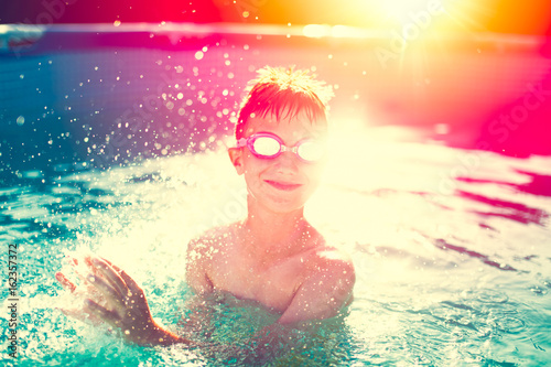 Little kid in goggles splashing in swimming pool, summer sunset, vintage