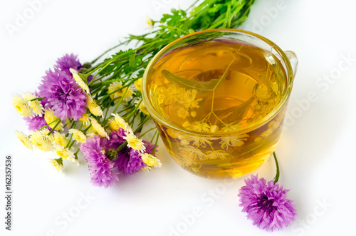 Natural therapy - Lime Tea in a transparent cup on a white background and a bouquet of wildflowers