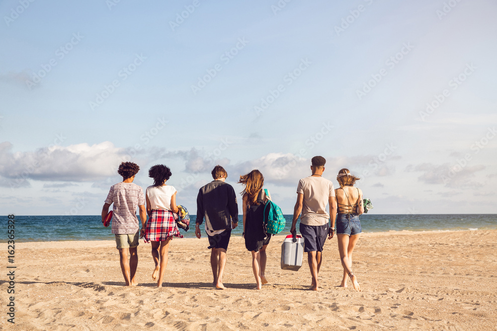 Young people walking on the beach carrying a cooler box Young people walking on the beach carrying a cooler box