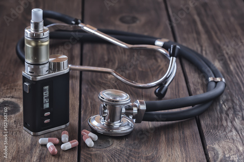 E- Zigarette zusammen mit einem Stethoskop und Medikamentenkapseln auf einer Holzunterlage