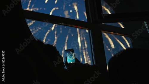 Girl taking fireworks video with a smartphone. Silhouette in a round loft window