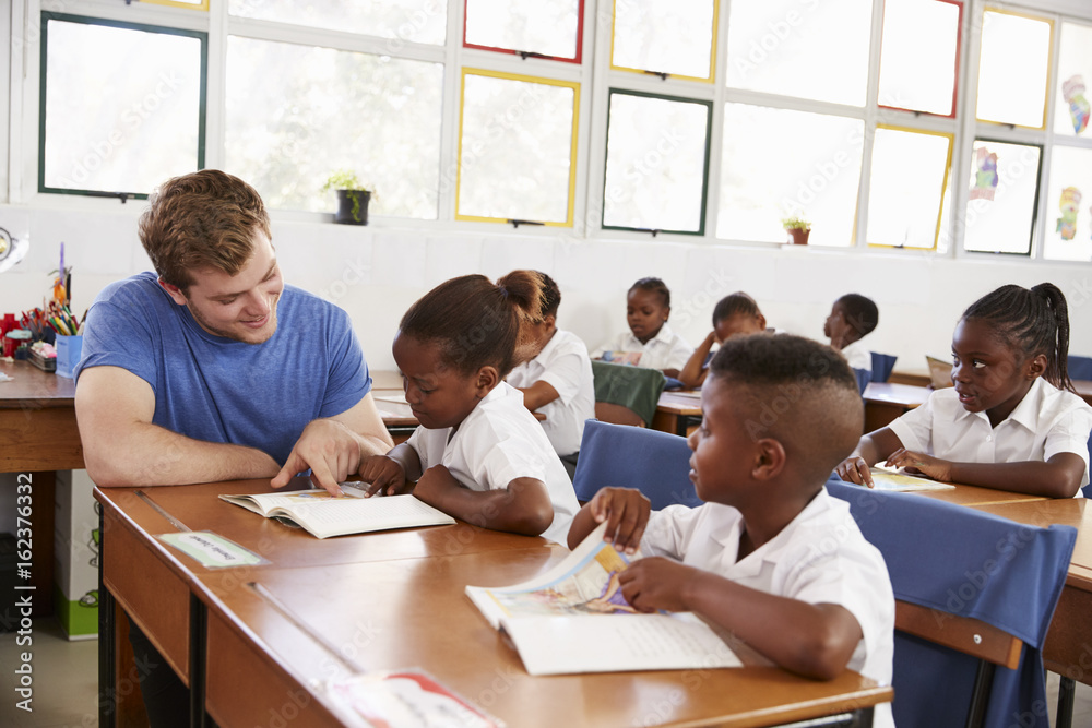 Volunteer teacher helping young girl at her desk in class Volunteer teacher helping young girl at her desk in class