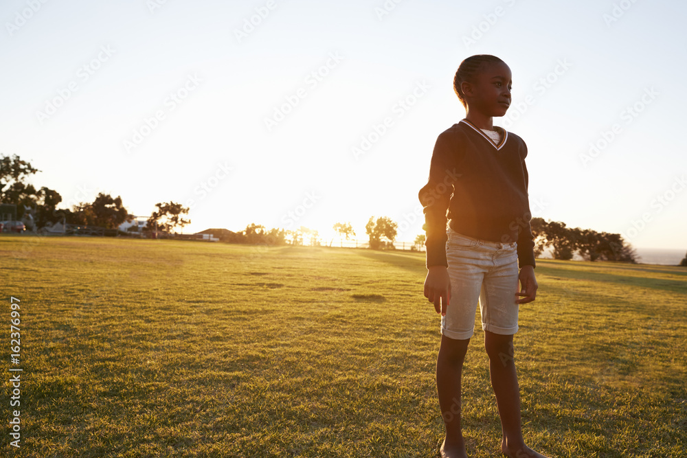 African elementary school girl standing in a park at sunset African elementary school girl standing in a park at sunset