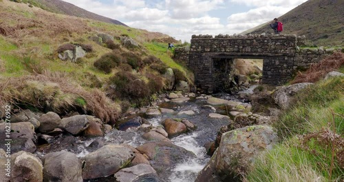 A hiker and their dog crossing an old stone bridge over Grainsgill Beck in the Caldbeck Fells in the English Lake District, UK. photo