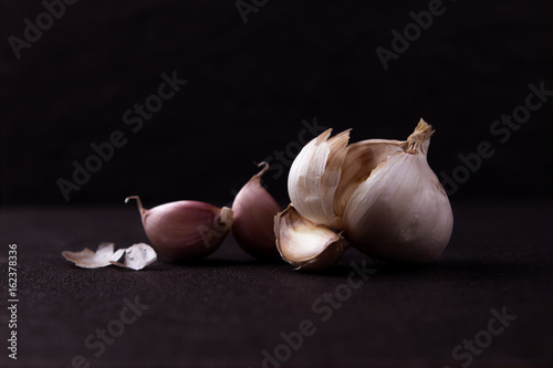  a still life arrangement of Three whole garlic bulbs grouped on black stone plate