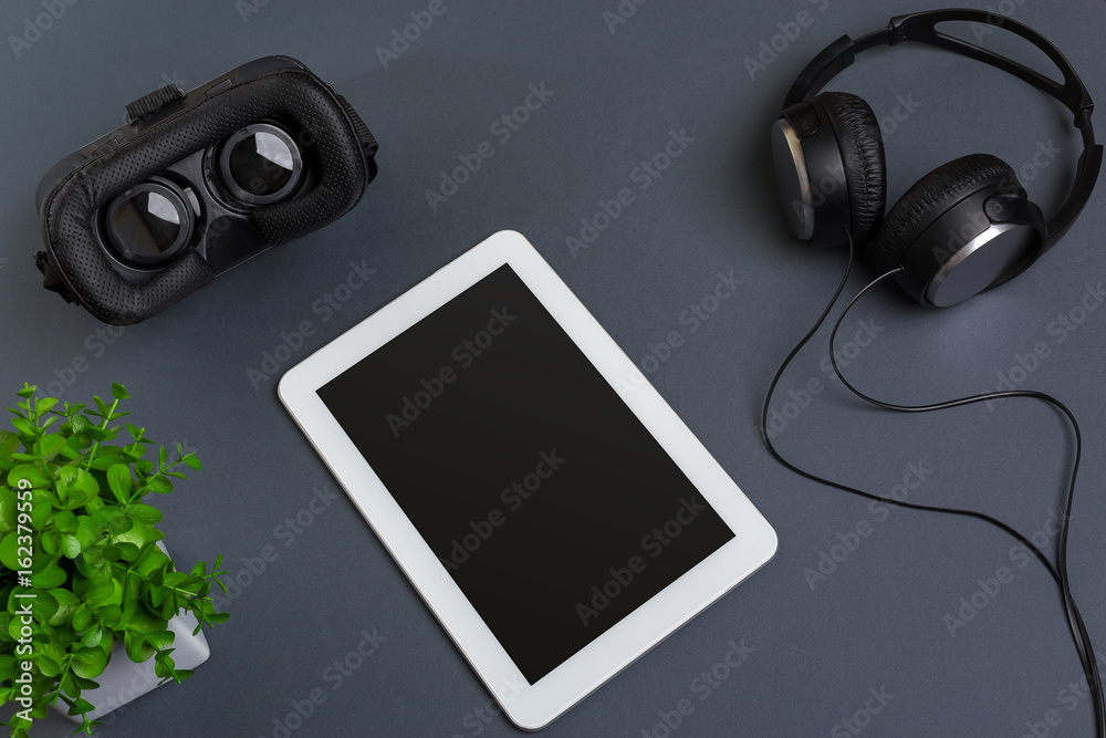 Virtual reality glasses and tablet with headphones on a gray background. Top view Virtual reality glasses and tablet with headphones on a gray background. Top view