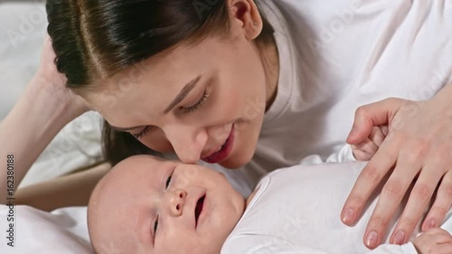 Closeup of happy mother kissing and nuzzling adorable baby on bed photo