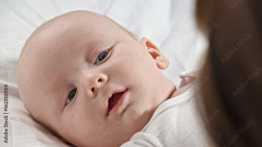 Top view of 2 months old baby lying on bed and looking at mother while she caressing him Top view of 2 months old baby lying on bed and looking at mother while she caressing him