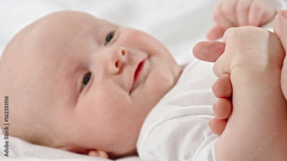 Closeup of adorable 2 months old baby lying on bed and holding finger of his mom Closeup of adorable 2 months old baby lying on bed and holding finger of his mom