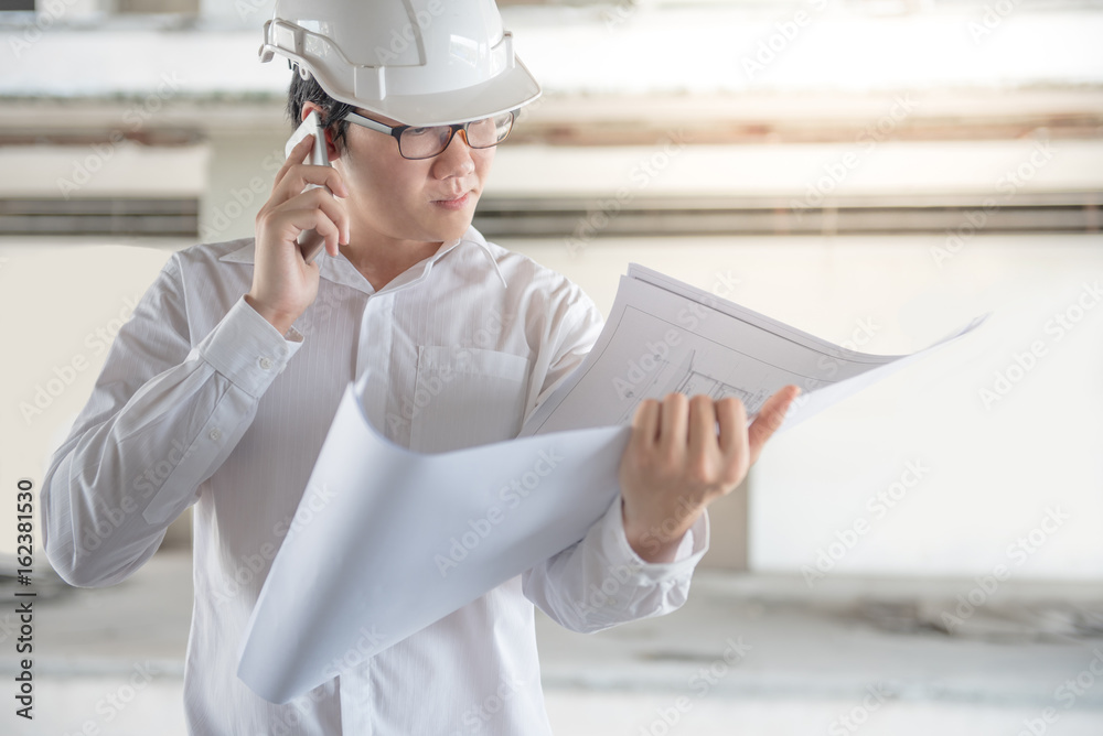 Engineer or Architect with protective safety helmet checking architectural drawing and calling support team at construction site. Engineering, Architecture and building construction concepts Engineer or Architect with protective safety helmet checking architectural drawing and calling support team at construction site. Engineering, Architecture and building construction concepts