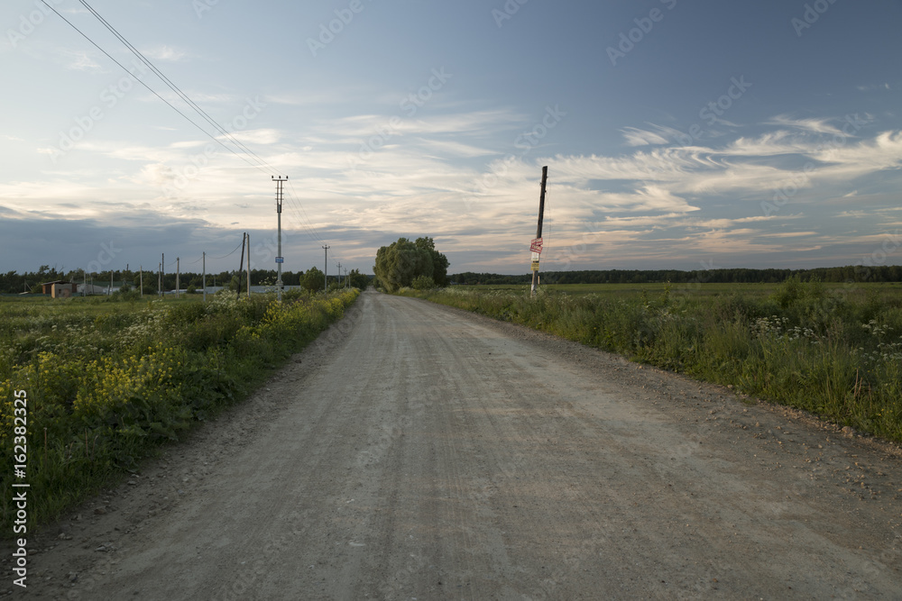 A dirt road through the field against the background of the evening sky.