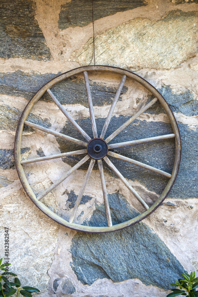 Old big wood wheel hanging on a stone wall from a farming house in Sweden