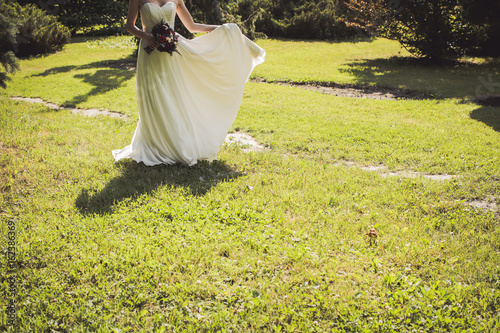 The bride stands on a clearing and holds a wedding bouquet
