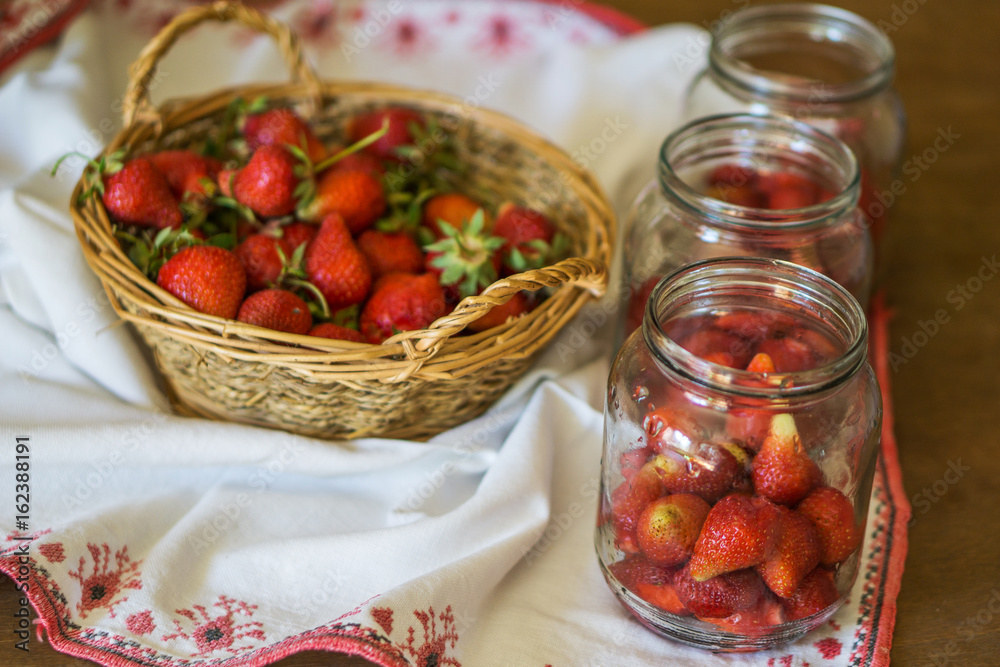 Close-up of strawberries for winter, jar and basket of fresh ripe fruit. Shallow depth of focus. Concept of home coziness. Close-up of strawberries for winter, jar and basket of fresh ripe fruit. Shallow depth of focus. Concept of home coziness.