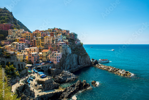 view of famous travel landmark destination Manarola, small mediterranean old sea town with harbour coast,Cinque terre National Park, Liguria, Italy. Summer sunny morning with tourists boat © ZoneCreative