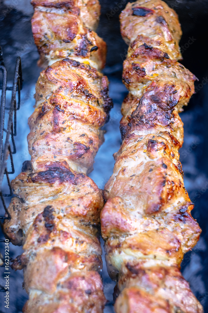 Marinated shashlik preparing on a barbecue grill over charcoal. Grilled kebab cooking on metal skewer. Roasted meat cooked at barbecue.