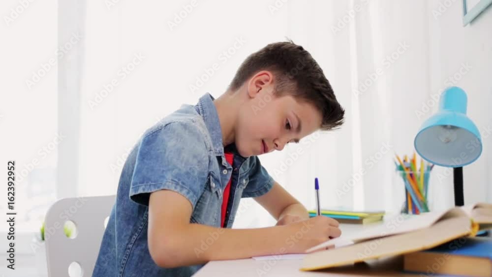 happy boy with book writing to notebook at home