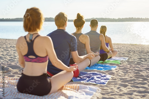 Row of young friends meditating on a beach