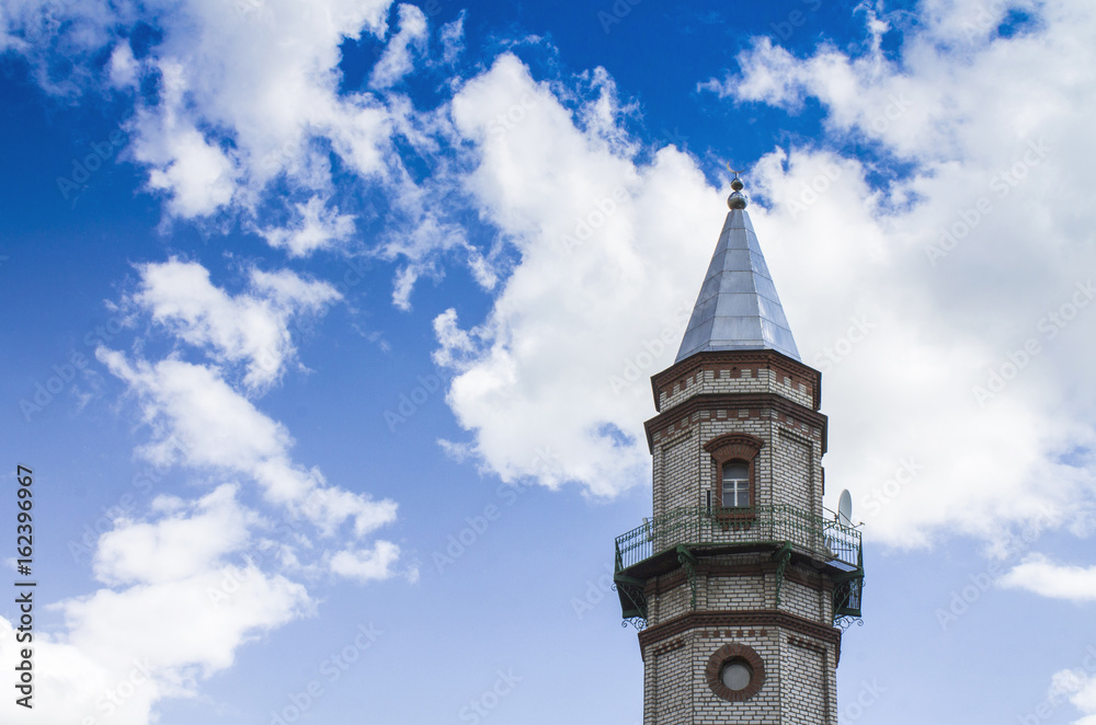 Mosque of Sunni Muslims. Minaret against the blue sky with white clouds.