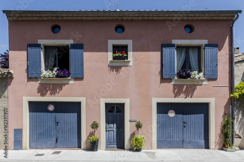 Pink french house in southern France with dark grey shutters and doors and flower pots at windows