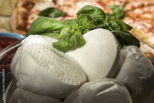 Mozzarelle di bufala Campana con foglie di Basilico e sullo sfondo una pizza margherita photo